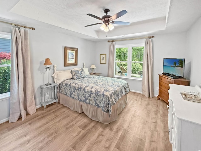 bedroom with light wood-style flooring, baseboards, a textured ceiling, and a raised ceiling