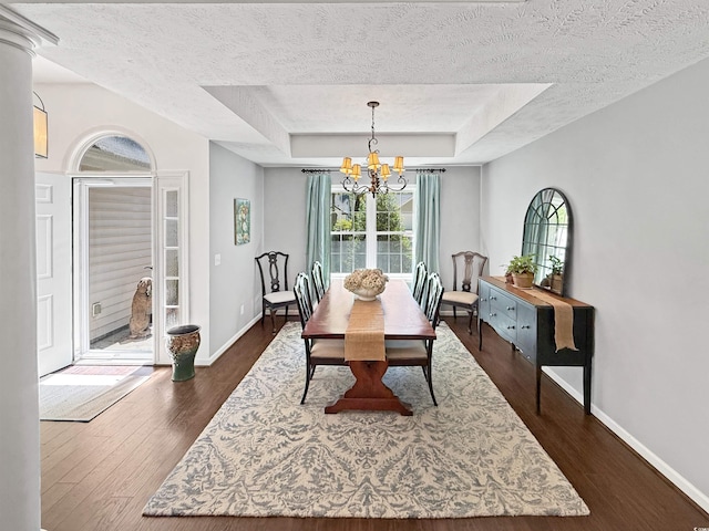 dining space featuring a raised ceiling, a textured ceiling, an inviting chandelier, and dark wood-type flooring