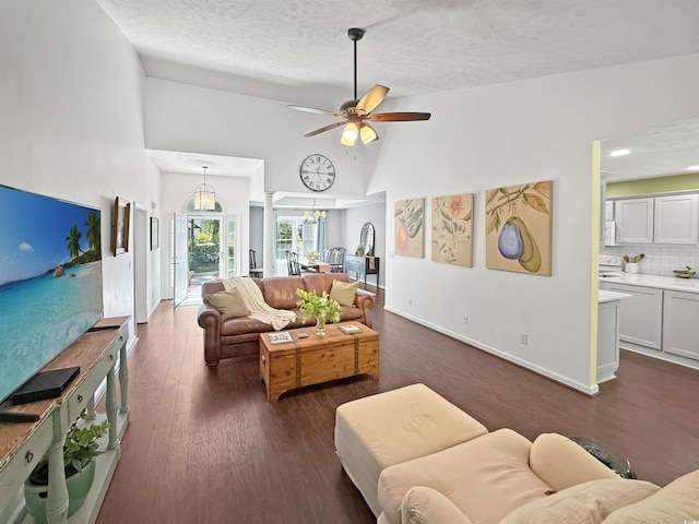 living area with a textured ceiling, dark wood finished floors, baseboards, ceiling fan with notable chandelier, and high vaulted ceiling