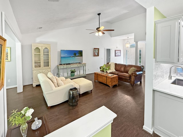 living room featuring dark wood-type flooring, baseboards, vaulted ceiling, and ceiling fan