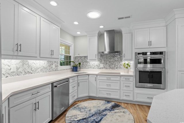 kitchen featuring visible vents, white cabinets, a sink, wall chimney range hood, and appliances with stainless steel finishes
