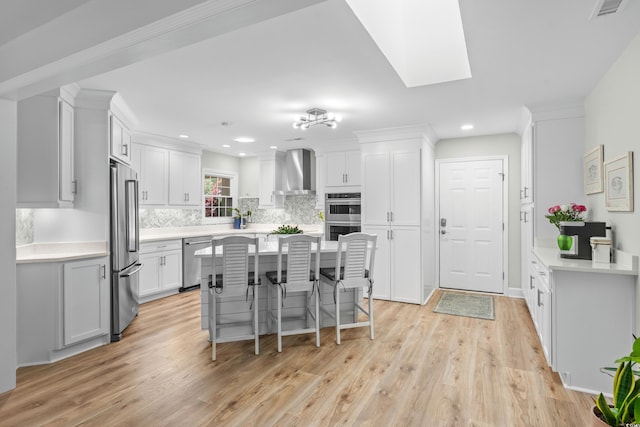 kitchen with light wood-style floors, appliances with stainless steel finishes, decorative backsplash, and wall chimney exhaust hood