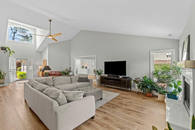 living room with high vaulted ceiling, light wood-type flooring, a ceiling fan, visible vents, and a premium fireplace
