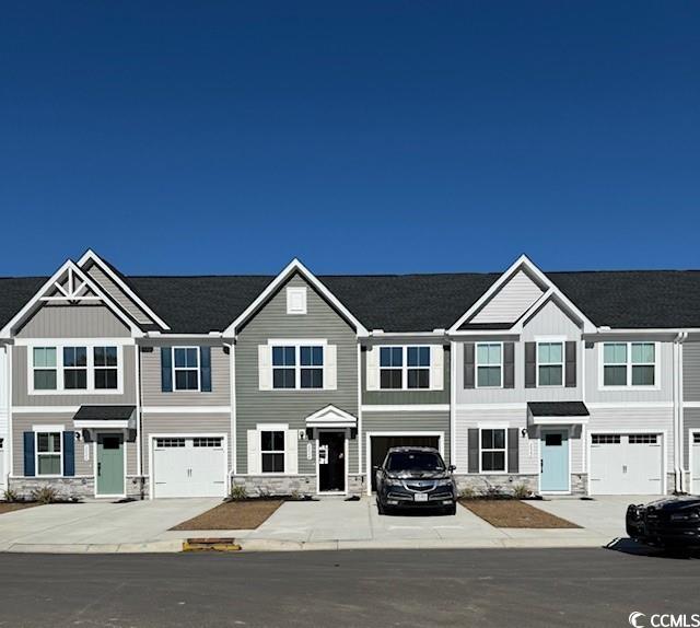 townhome / multi-family property featuring a garage, stone siding, and driveway