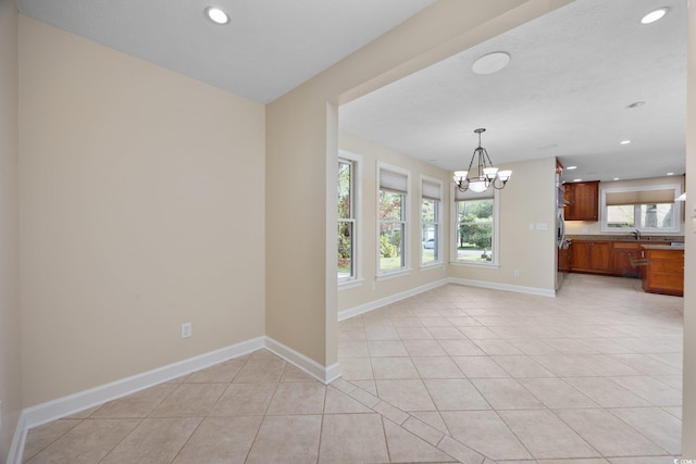 unfurnished living room with a chandelier, light tile patterned flooring, baseboards, recessed lighting, and a sink