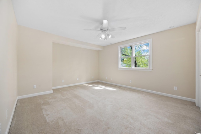 spare room with a ceiling fan, baseboards, and light carpet