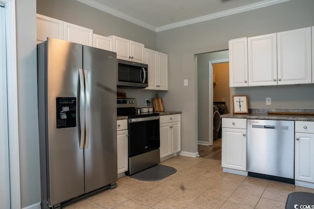 kitchen with appliances with stainless steel finishes, independent washer and dryer, dark countertops, ornamental molding, and white cabinets