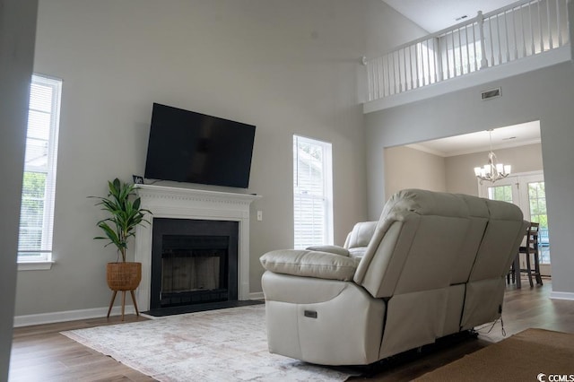 living room featuring wood finished floors, a chandelier, crown molding, baseboards, and a fireplace with flush hearth