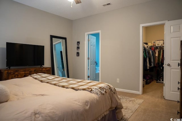 bedroom with a walk in closet, light colored carpet, a closet, baseboards, and ensuite bath