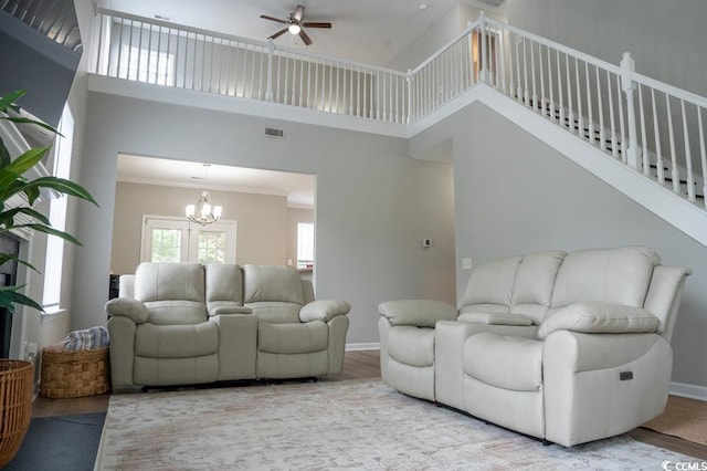 living room featuring a chandelier, a ceiling fan, a towering ceiling, ornamental molding, and baseboards