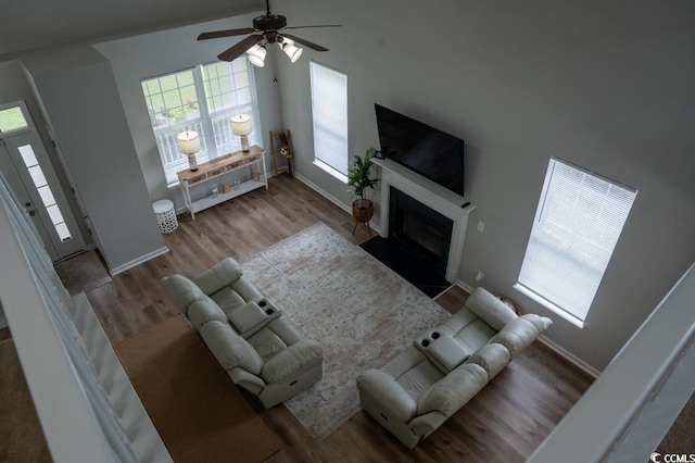 living area with a ceiling fan, wood finished floors, baseboards, and a fireplace with flush hearth