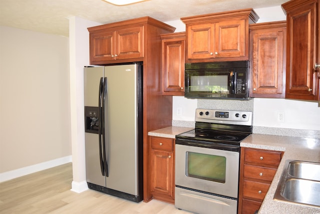 kitchen with light wood finished floors, appliances with stainless steel finishes, brown cabinetry, and light countertops
