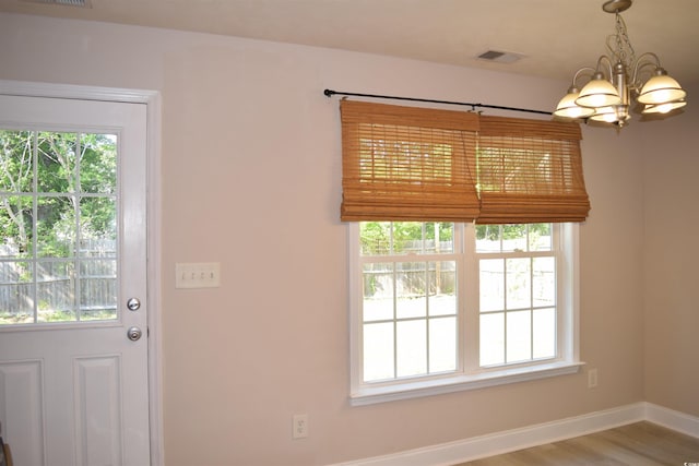 doorway to outside featuring a notable chandelier, visible vents, wood finished floors, and baseboards