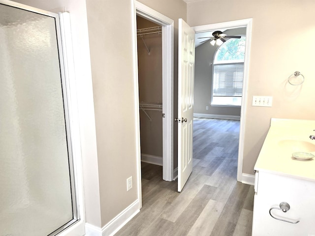 full bath featuring a shower stall, wood finished floors, ceiling fan, and a spacious closet