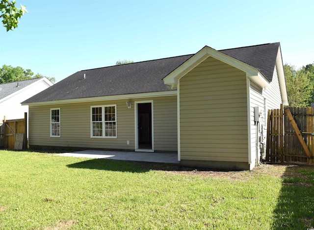 rear view of property with a patio, a lawn, a shingled roof, and fence