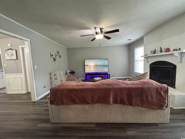 living area with a textured ceiling, a brick fireplace, wood finished floors, ceiling fan, and ornamental molding