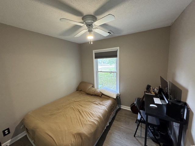 bedroom with a ceiling fan, wood finished floors, visible vents, and a textured ceiling