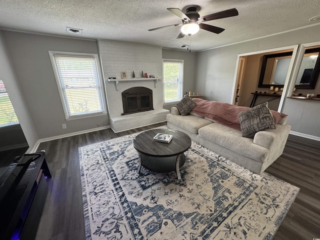 living room featuring a textured ceiling, ceiling fan, dark wood finished floors, a brick fireplace, and visible vents