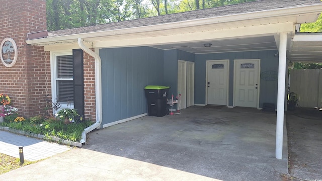view of exterior entry with driveway, an attached carport, brick siding, and roof with shingles