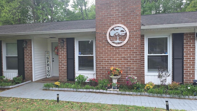 view of exterior entry with brick siding, roof with shingles, and a chimney