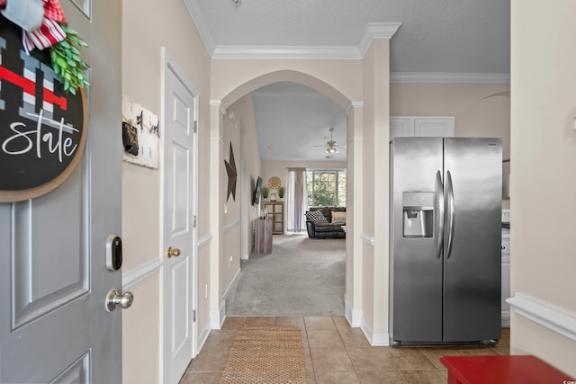 corridor featuring arched walkways, ornamental molding, light tile patterned floors, light carpet, and baseboards