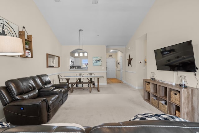 living area featuring arched walkways, light carpet, baseboards, and high vaulted ceiling