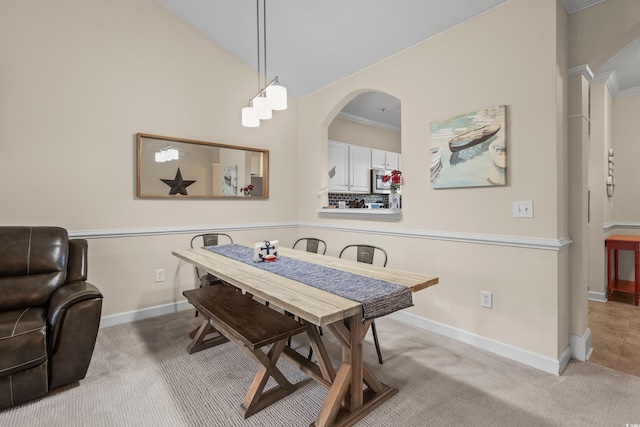 carpeted dining space featuring arched walkways, baseboards, lofted ceiling, and crown molding