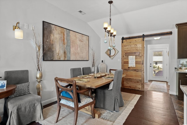 dining space with a barn door, vaulted ceiling, and wood finished floors