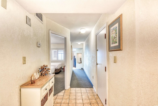 hall featuring light tile patterned floors, a textured wall, and visible vents