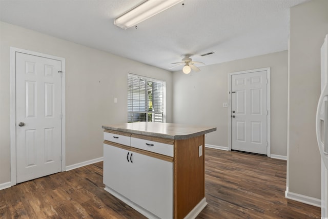 kitchen with dark wood finished floors, a ceiling fan, visible vents, a kitchen island, and baseboards