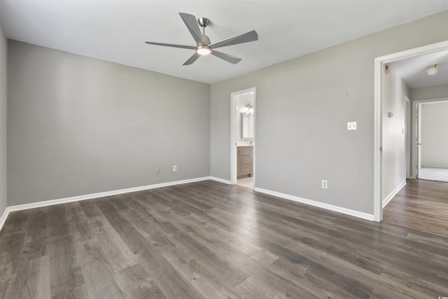 unfurnished bedroom with dark wood-style flooring, ensuite bathroom, baseboards, and a ceiling fan
