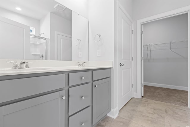 bathroom with double vanity, a walk in closet, a shower, and baseboards