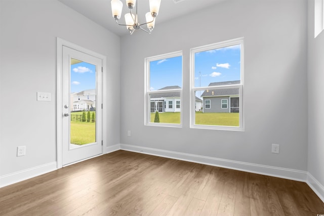 unfurnished dining area with a chandelier, wood finished floors, and baseboards