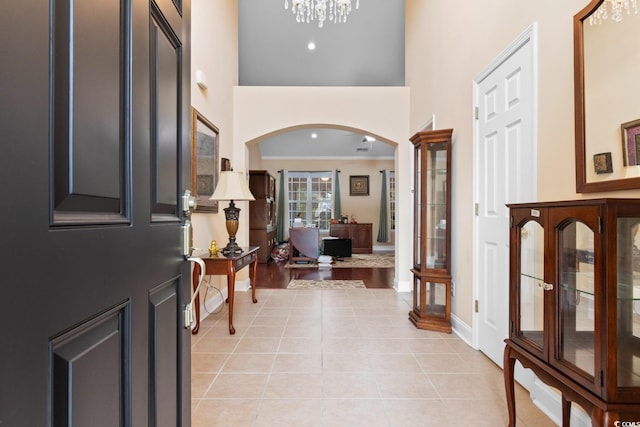 foyer with light tile patterned floors, arched walkways, a notable chandelier, crown molding, and a towering ceiling