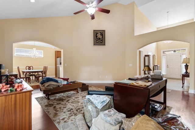 living room featuring high vaulted ceiling, arched walkways, wood finished floors, and ceiling fan with notable chandelier