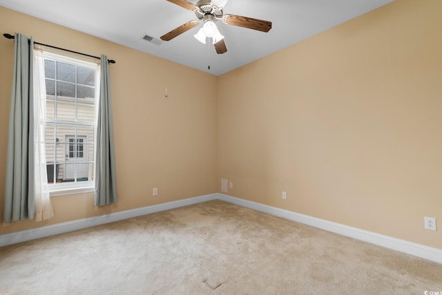 spare room with light colored carpet, baseboards, a ceiling fan, and visible vents
