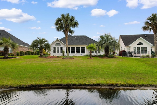rear view of house with a water view, fence, and a lawn