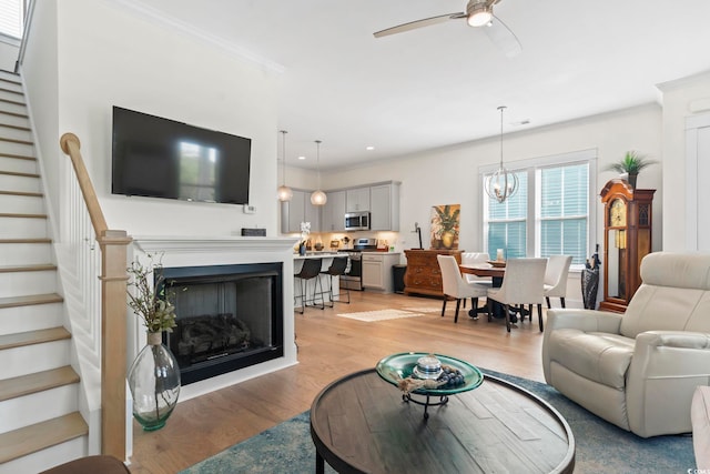 living area featuring light wood finished floors, recessed lighting, ceiling fan with notable chandelier, stairs, and ornamental molding