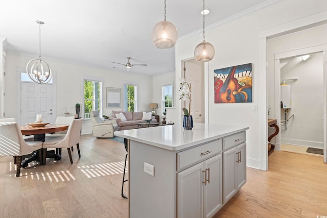 kitchen with ceiling fan with notable chandelier, light wood-style floors, a healthy amount of sunlight, light countertops, and a kitchen island