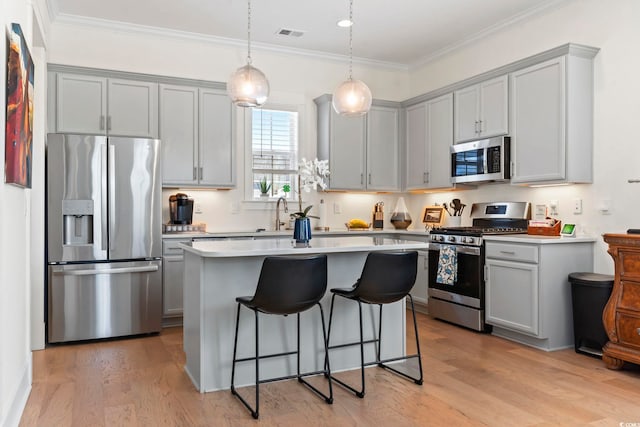 kitchen with light wood finished floors, a breakfast bar, gray cabinetry, and appliances with stainless steel finishes