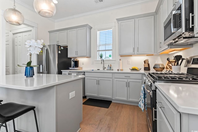 kitchen with ornamental molding, a sink, light wood-style floors, a kitchen bar, and appliances with stainless steel finishes