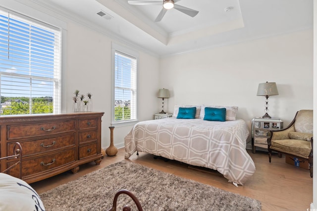 bedroom featuring a raised ceiling, wood finished floors, visible vents, a ceiling fan, and crown molding
