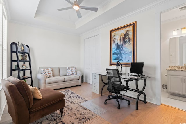 office with light wood finished floors, a raised ceiling, a ceiling fan, crown molding, and baseboards