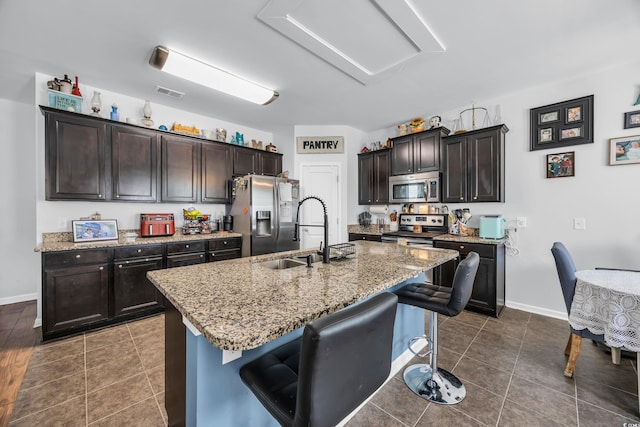 kitchen featuring a sink, a center island with sink, light stone counters, a breakfast bar, and appliances with stainless steel finishes