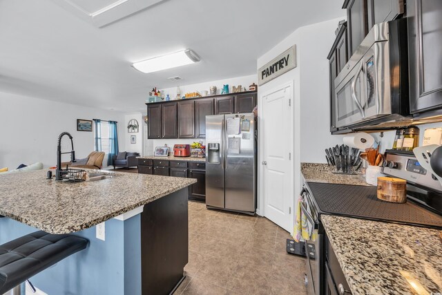 kitchen with a sink, appliances with stainless steel finishes, light stone counters, a breakfast bar, and light tile patterned floors