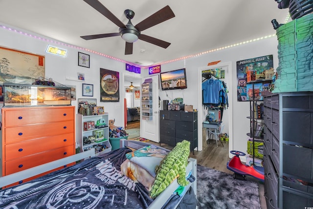 bedroom featuring a walk in closet, wood finished floors, a closet, and ceiling fan
