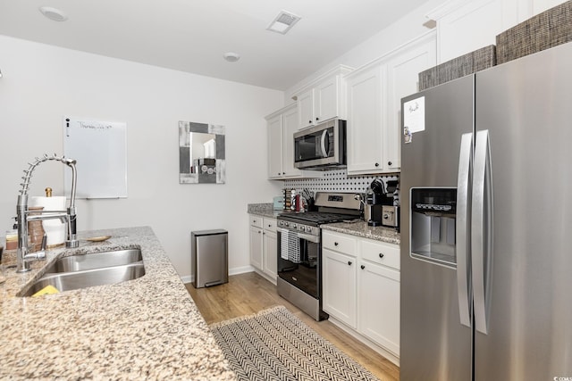 kitchen featuring light wood finished floors, a sink, stainless steel appliances, visible vents, and white cabinetry