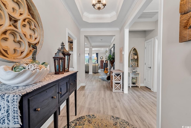 foyer with a tray ceiling, light wood finished floors, baseboards, ornamental molding, and visible vents