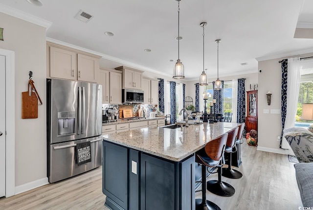 kitchen featuring a sink, an island with sink, stainless steel appliances, light wood finished floors, and ornamental molding