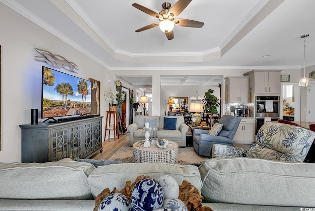 living area featuring a tray ceiling, light wood-style flooring, ornamental molding, and ceiling fan